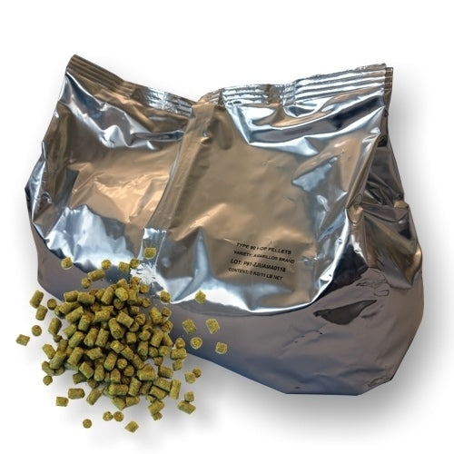 En sølvglinsende foliepose med Yakima Valley Hops Zappa 5 kg humlepellets 2020 (2,6 %) med grønngule pellets som sprer seg på en hvit overflate.
