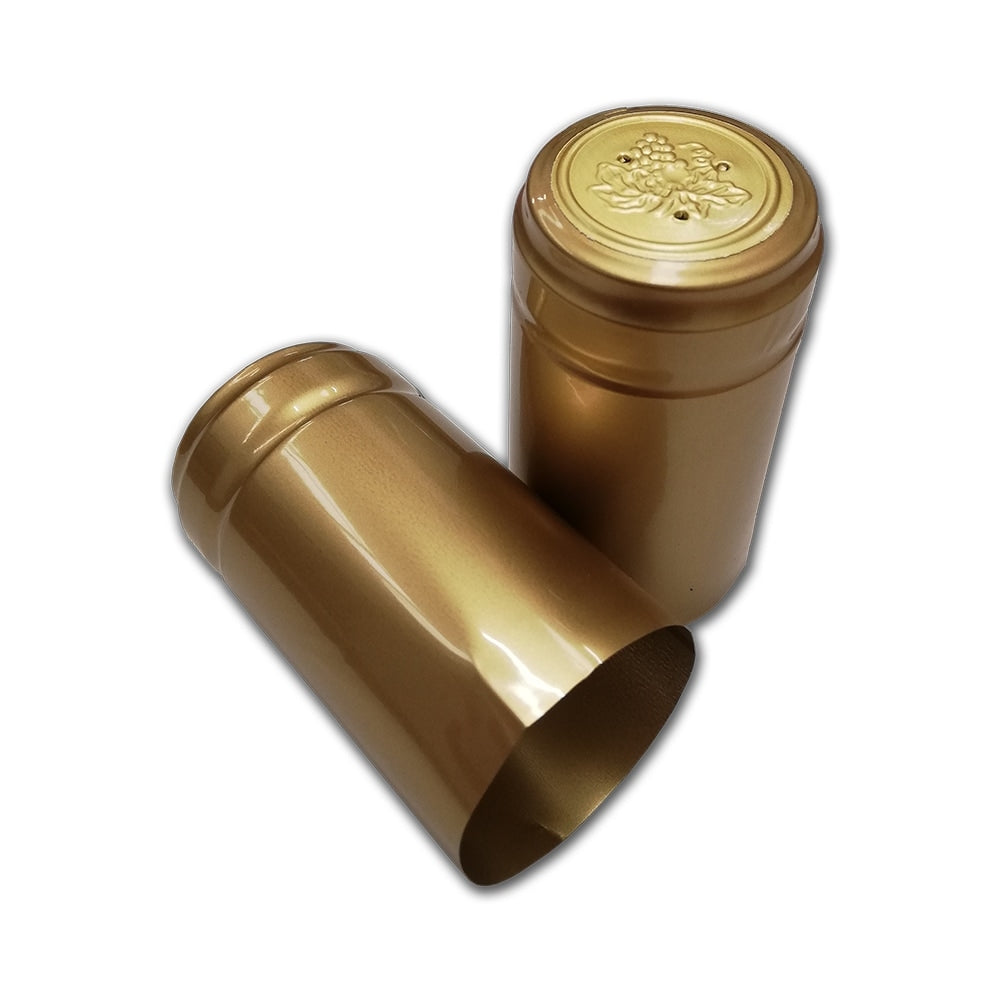 To Gull krympehetter til vinflasker (30 stk.) i metallisk gull fra Handcraft Supplies Gull krympehetter til vinflasker (30 stk.): den ene stående med druemotiv på toppen, den andre liggende på siden.