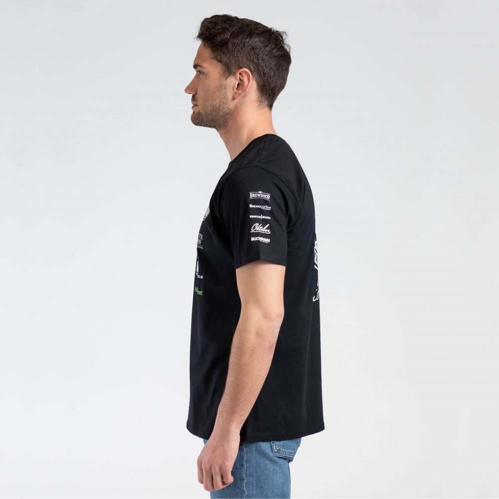 En mann i profil med ansiktet vendt mot venstre, iført Brewshop Craft Brewers Team T-skjorte - Unisex med hvit tekst og blå jeans mot en vanlig hvit bakgrunn.