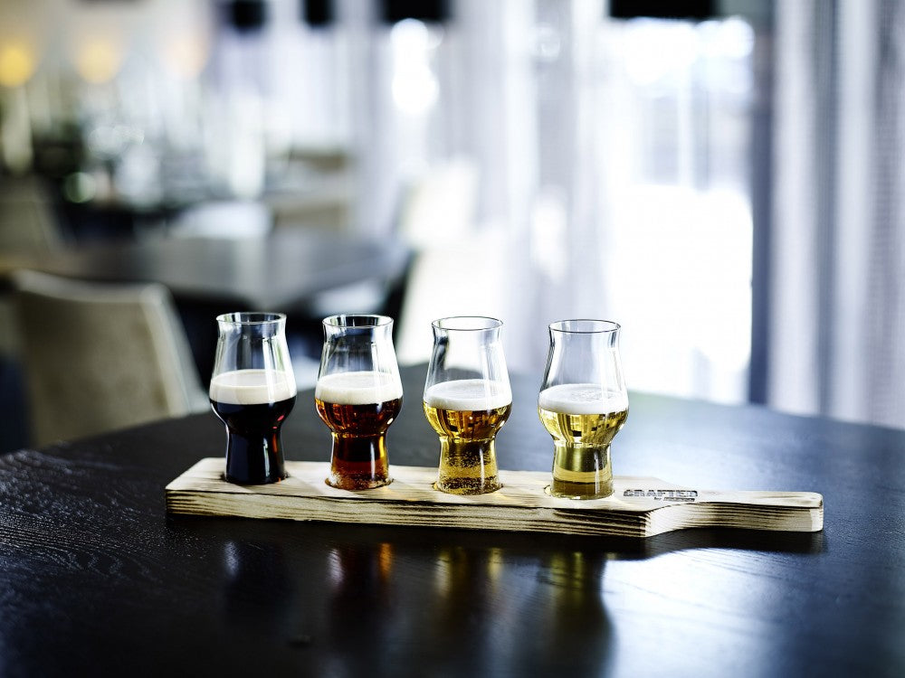 Rastal Craft Beer Paddle - Smaksplanke for Craft Master One Taster fra Rastal har plass til fire smaksprøver med øl i ulike farger, plassert på et mørkt bord i en moderne, svakt opplyst atmosfære.