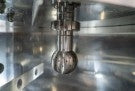 Nærbilde av en metallisk industrikomponent med bolter og sylindere inne i et reflekterende kammer, en del av EnoBeer Enobrau 500 Professional Flame gassfyrt brygghus med EnoBrew-Touch kontrollpanel.