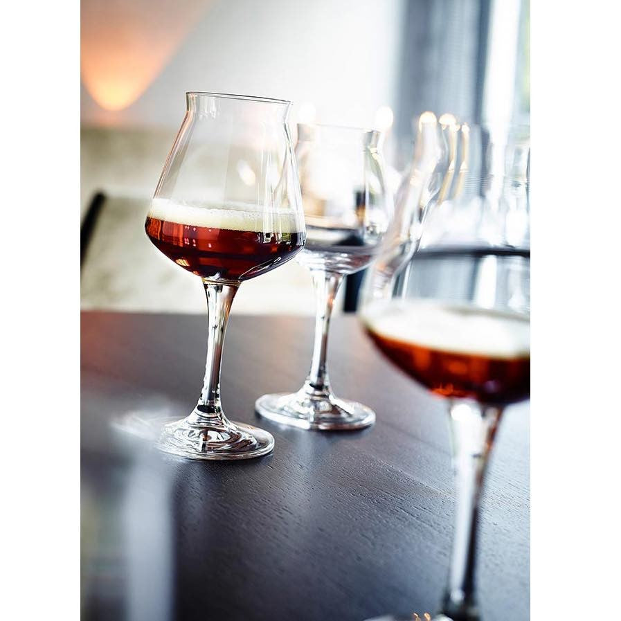 Seks Rastal TEKU 3.0 42 cl ølglass fra Rastal, hvert fylt med en mørk, ravfarget øl og toppet med skum, er plassert på et mørkt trebord i en dempet belysning.