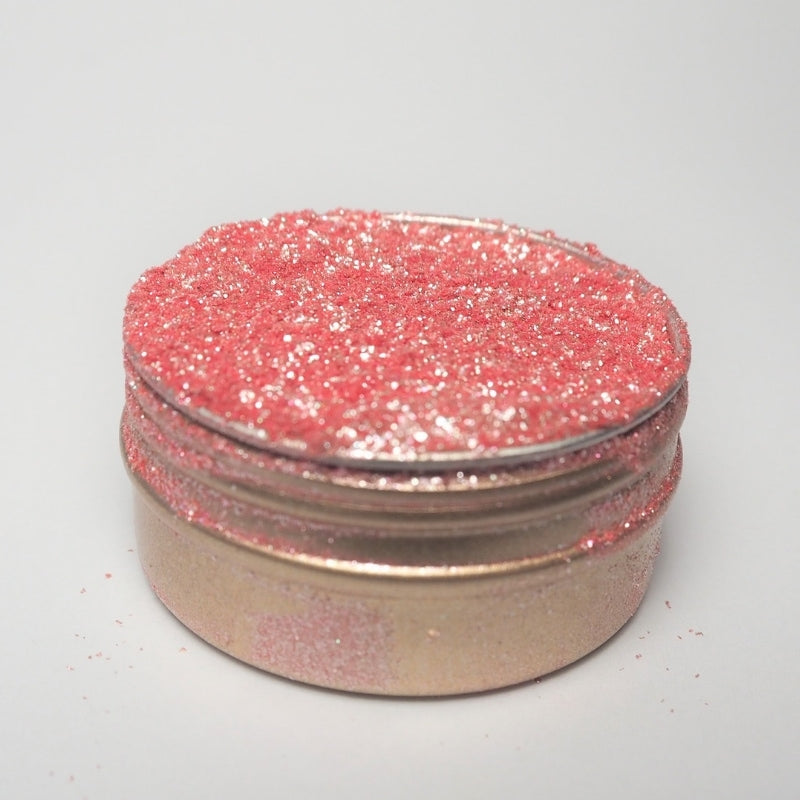 En liten rund beholder med Eco Lovers Eat Me Glitter Rose 20 ml, fylt med rosa spiselig glitter og litt spredt på lokket og sidene, perfekt til kakepynt, er satt mot en vanlig hvit bakgrunn.