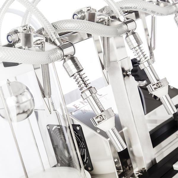 Nærbilde av den halvautomatiske vakuumflaskefylleren Enolmaster for brennevin fra Tenco, som fremhever metalldysene, de gjennomsiktige rørene og de presise mekaniske komponentene.