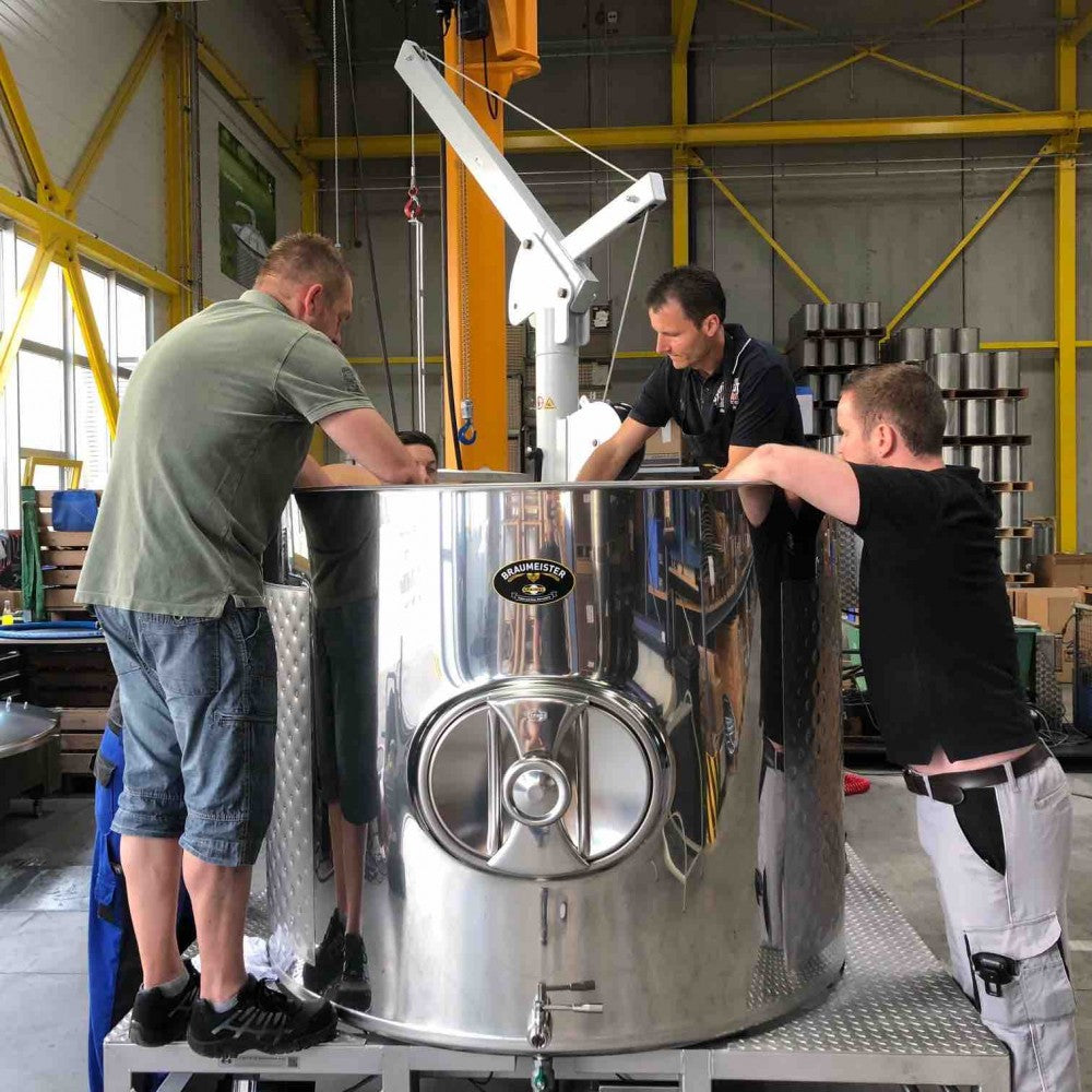 Fire menn inspiserer Speidel #Braumeister 1000L - Bestillingsvare, et stort automatisk bryggesystem fra Speidel, inne på en fabrikk som viser den imponerende skalaen for kommersiell ølbrygging.