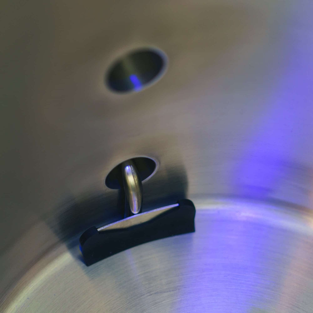 Nærbilde av Ss Brewtech Ss TC Brew Kettle 189L (50 gal) Bryggekjele, som viser en nagle og et svart håndtak, med blå og lilla refleksjoner som virvler på overflaten i rustfritt stål.