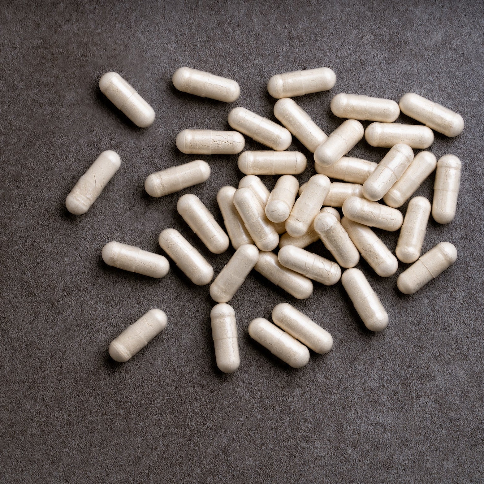 En gruppe hvite kapsler, for eksempel Lallemand Servomyces Blister Pack Gjærnæring – 10 kapsler, spredt utover en mørk, strukturert overflate – ideelt for optimale bryggingsresultater.