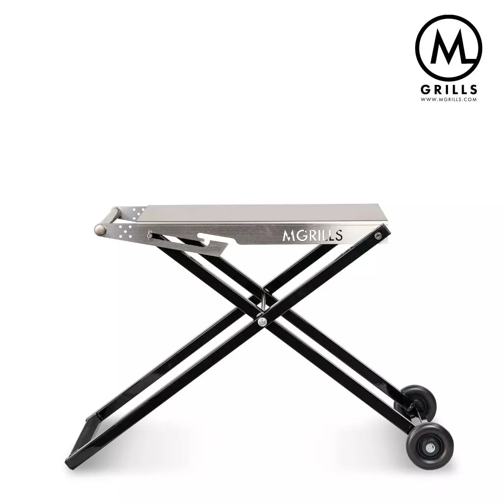 C4 Folding Cart fra M Grills er et bærbart bord av rustfritt stål for M16, med svarte, sammenleggbare ben, to hjul og M Grills-logo på både grillen og øverst i høyre hjørne.