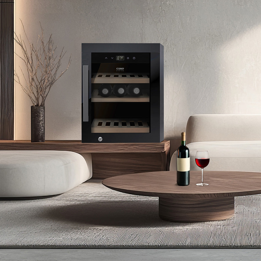 En moderne stue med et kompakt Caso WineExclusive 12 frittstående vinkjøleskap, et rundt salongbord i tre med en flaske rødvin og et glass på, samt minimalistiske møbler.