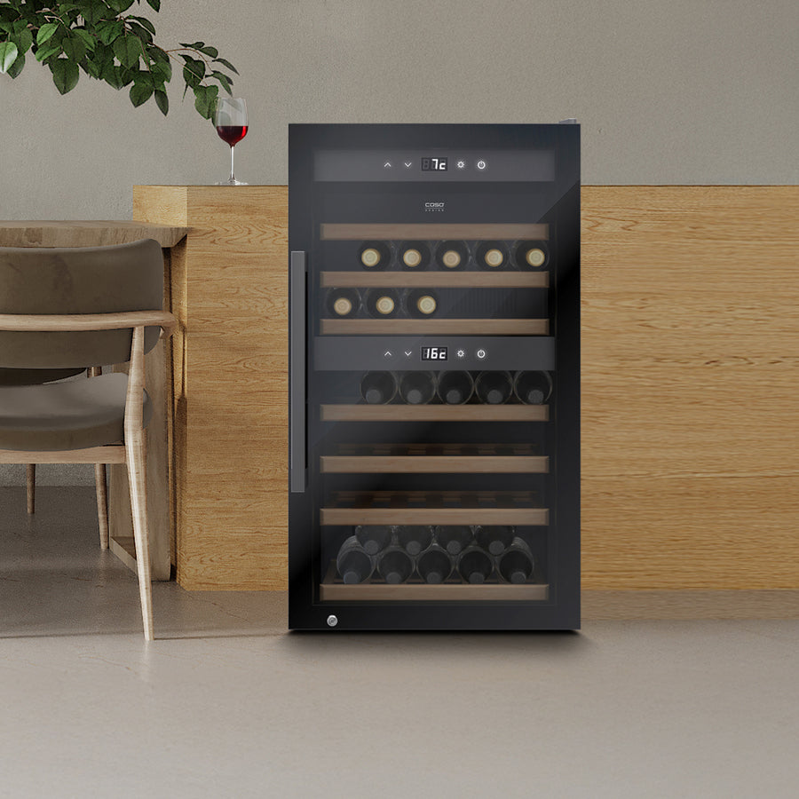 Foran en trebenk står Caso WineExclusive 66 Smart Falstaff Edition frittstående vinkjøleskap, og gjennom glassdøren kan man se flaskene som står på elegante trehyller. Et glass rødvin står på disken, med en stol plassert til venstre. Dette sofistikerte vinskapet har to temperatursoner, slik at vinene dine oppbevares ved optimal temperatur.