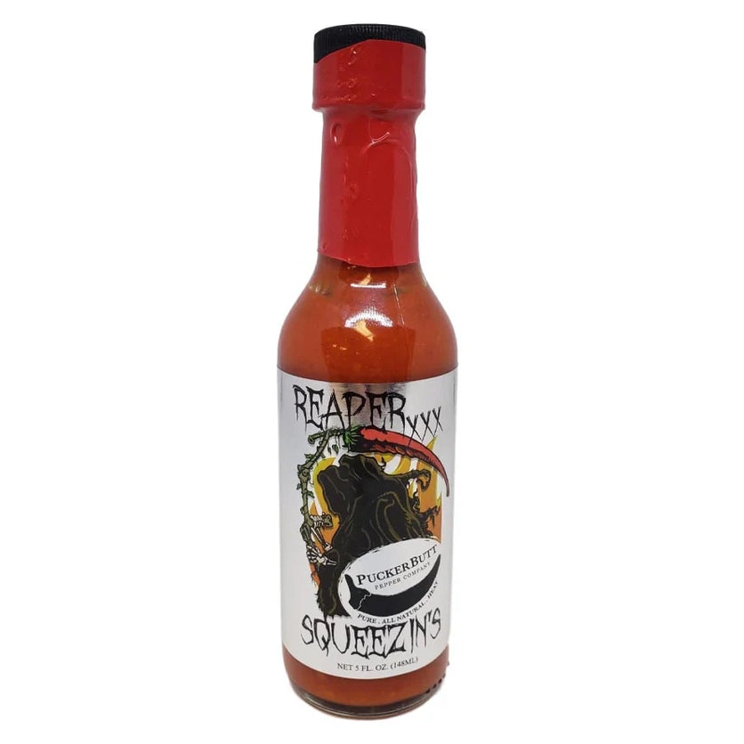 En flaske PuckerButt Pepper Company Extra Hot Reaper Squeezins Sauce har en rød hetelokk og fet, mørk grafikk på etiketten; denne limited edition Carolina Reaper hot sausen leverer intens hete.