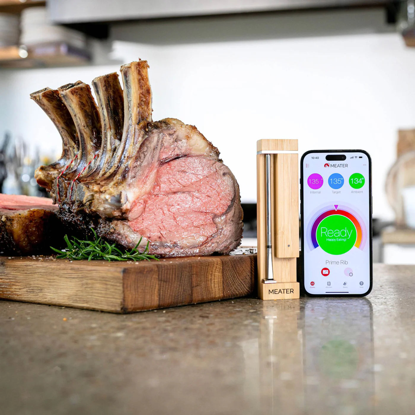 En stekt ribbe hviler på et trebrett ved siden av et Traeger Meater Pro - Bluetooth-steketermometer og en smarttelefon som viser hvordan tilberedningen går.