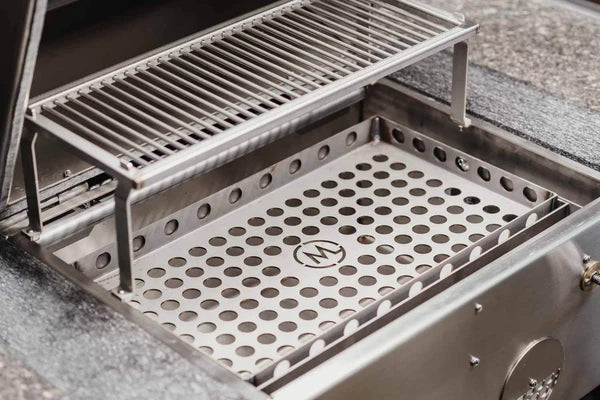M Grills B24 kullgrill av rustfritt stål med to-nivåers kokegrill, justerbar kullrist og perforert brett med sirkulær logo i midten.