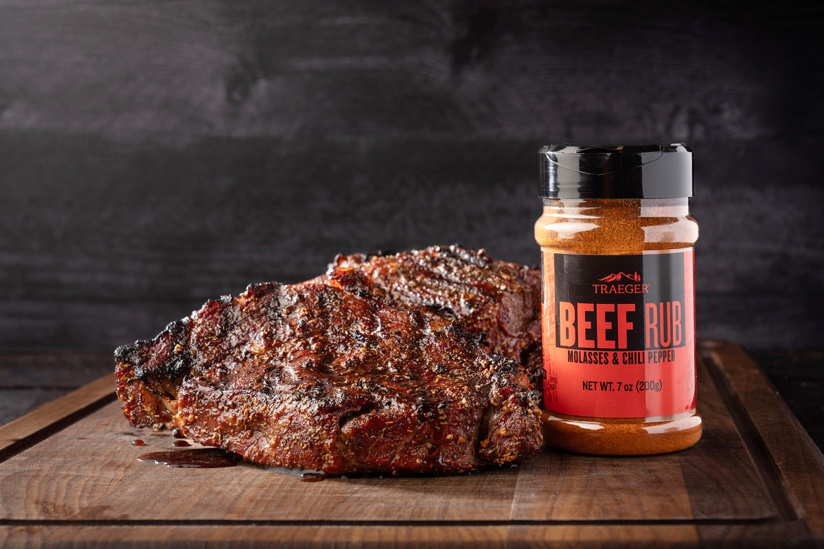 En grillet storfekjøttbiff hviler på et skjærebrett av tre ved siden av en krukke med Traeger Beef Rub 200g fra Traeger.