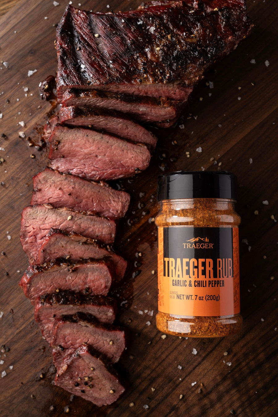 Skiver av grillet biff på et trebrett ved siden av en krukke med Traeger Rub 200 g fra Traeger - ideell til å fremheve kjøttretter.