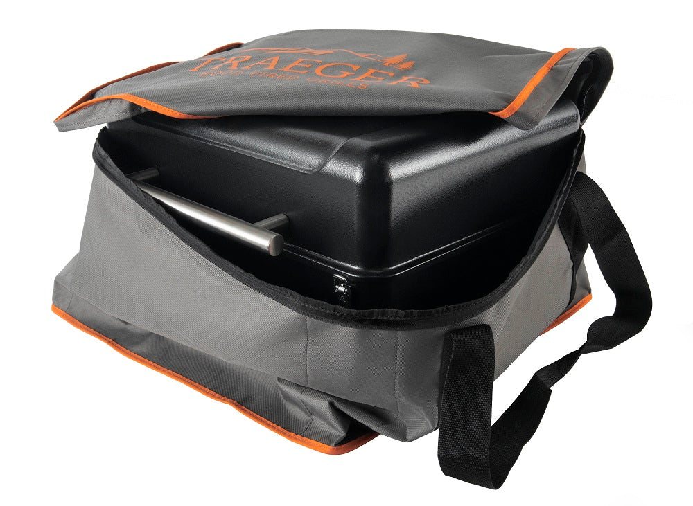 En Traeger Ranger-grill ligger delvis inne i Traeger To-Go Bag fra Traeger, som har oransje kanter, en skulderrem og en åpen topp som avslører den bærbare grillen og metallhåndtaket. Vesken er også værbestandig.