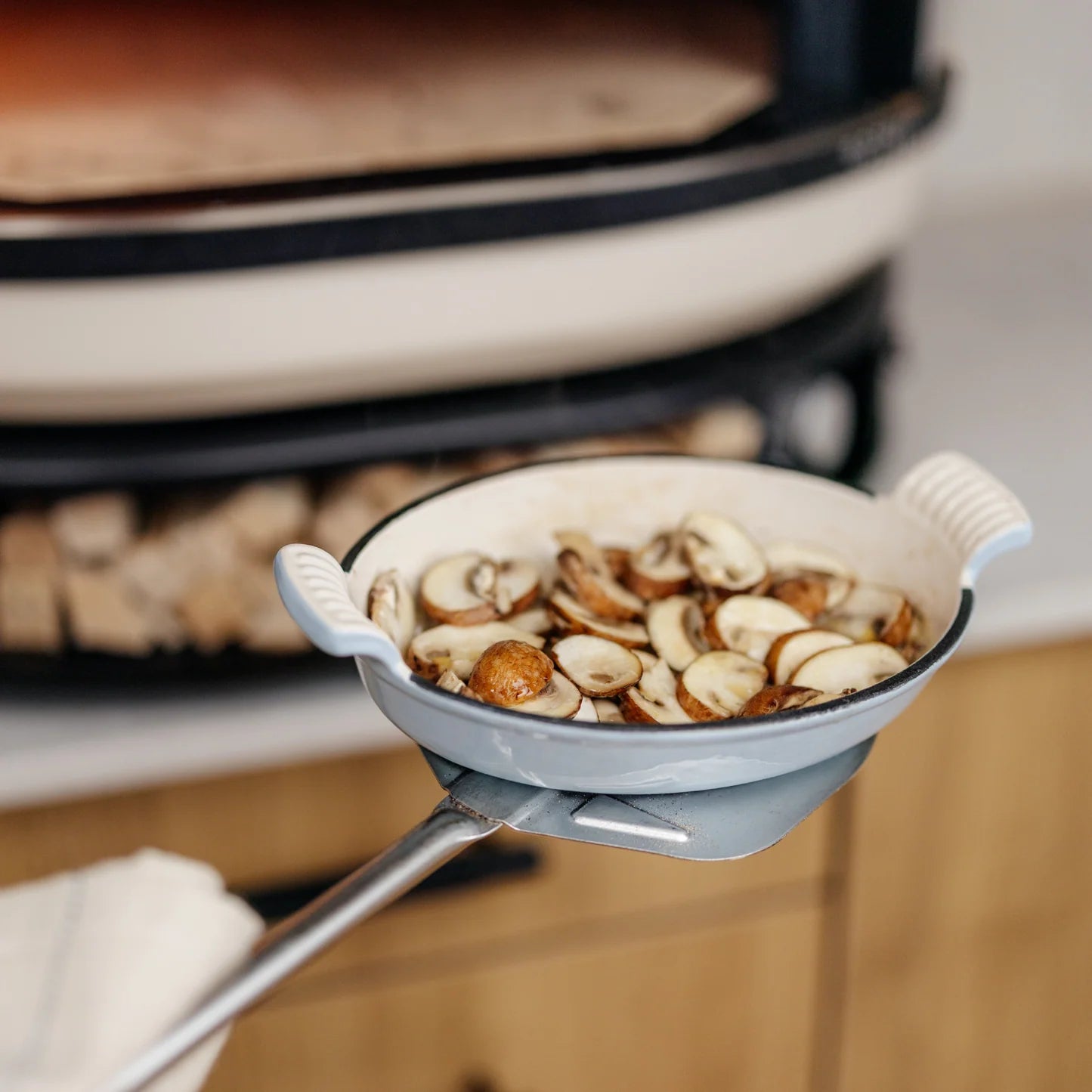 En hvit bakeform fylt med oppskåret sopp ligger på Gozney Utility Turning Peel, klar for åpen ovn - et praktisk Gozney pizzatilbehør for enhver hjemmekokk.