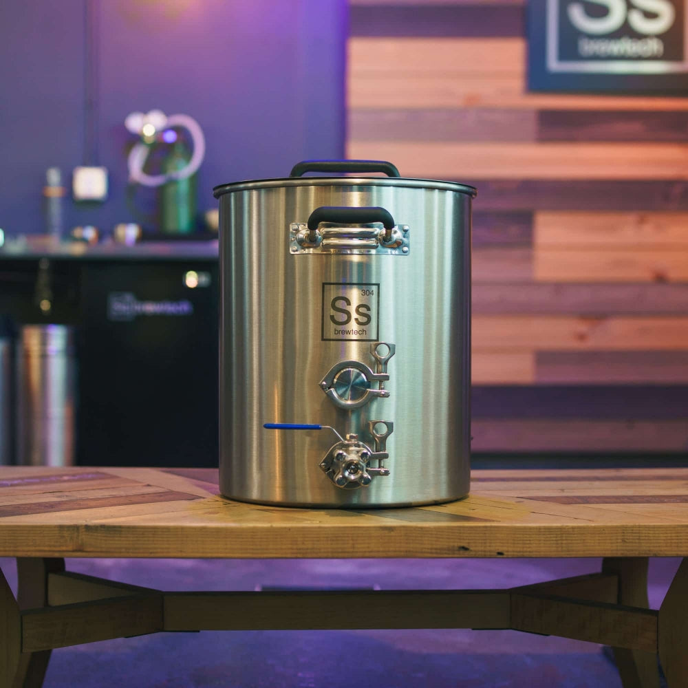 En Ss Brewtech TC Brew Kettle 189L (50 gal) Bryggekjele står på et trebord i et moderne innendørslokale, omgitt av bryggeutstyr og plassert mot en trevegg.