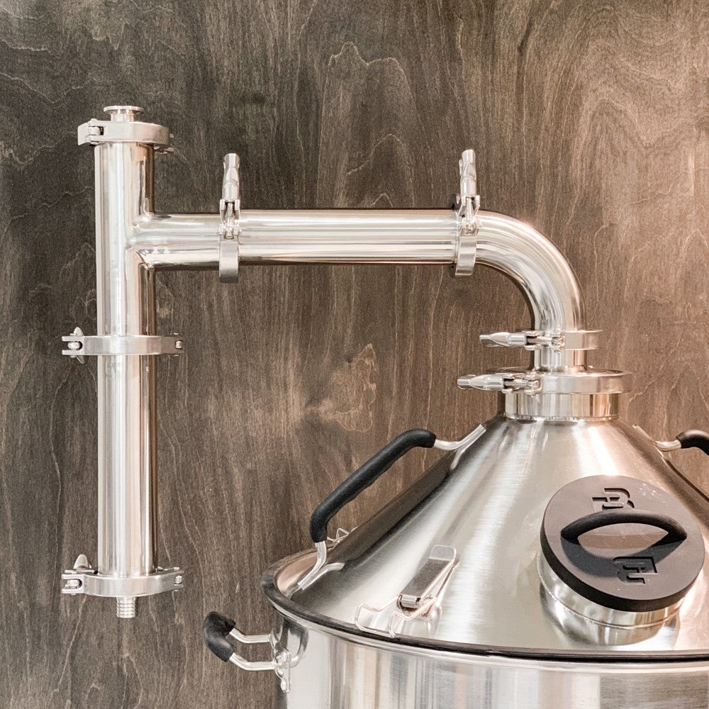 Brewtools Dampkondensator til Brewtools er en destillasjonskolonne i rustfritt stål montert på en håndtert metalltank, vist mot en bakgrunn i tremønster - ideell for avanserte ølbryggingsoppsett.
