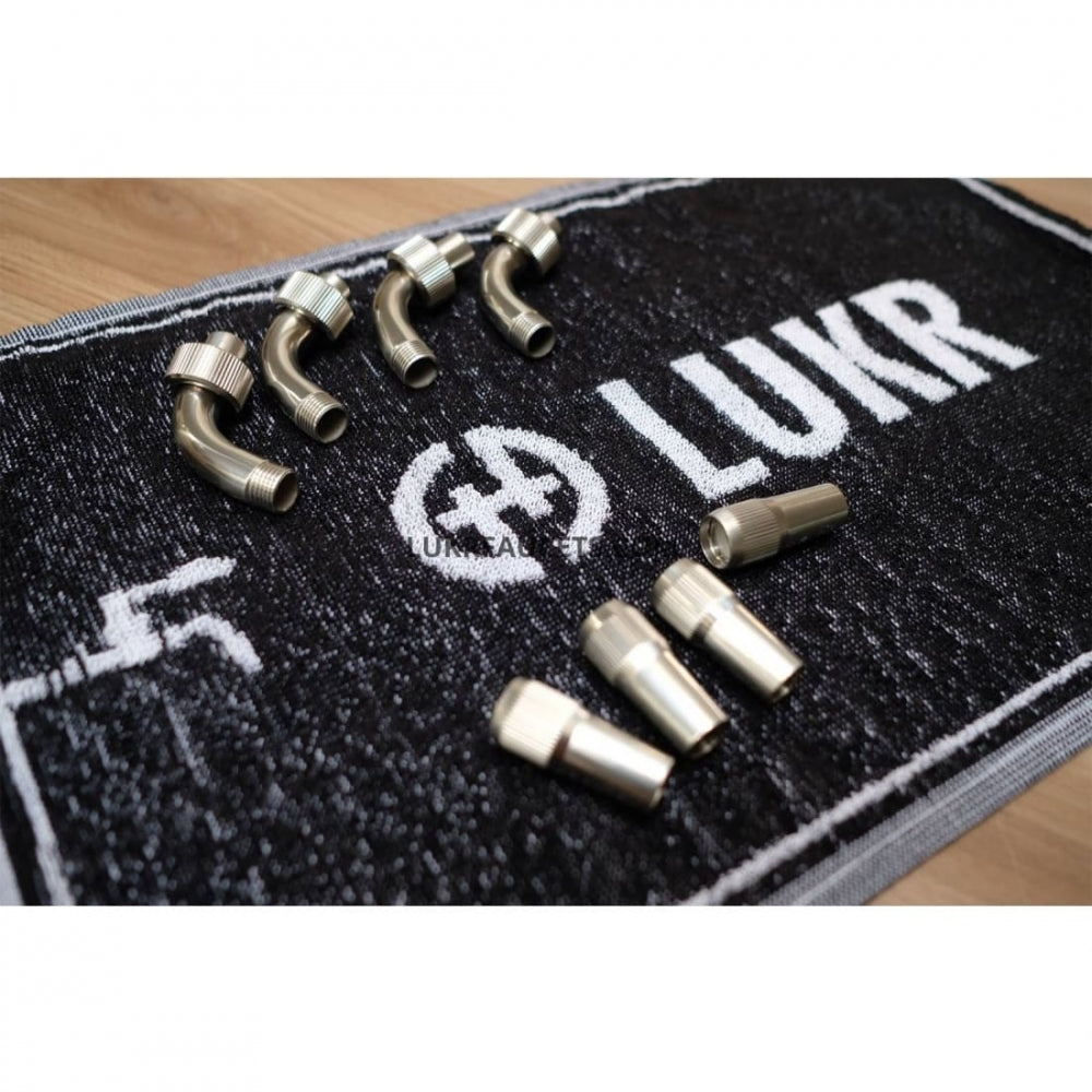 En samling av vinklede og rette metallbeslag vises på et svart LUKR Bar Towel (50x30 cm, bomull) med Lukr-merkenavnet og kranens symbol.