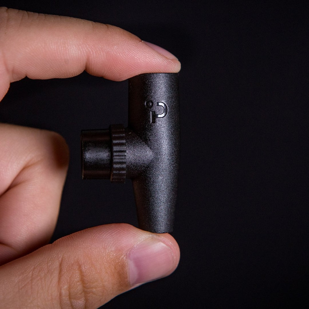 En hånd holder en Plaato PLAATO Valve V2 - Pressure Drop Equalizing Valve, en liten, svart enhet med en sylindrisk forlengelse og bokstaven G på siden, mot en svart bakgrunn.