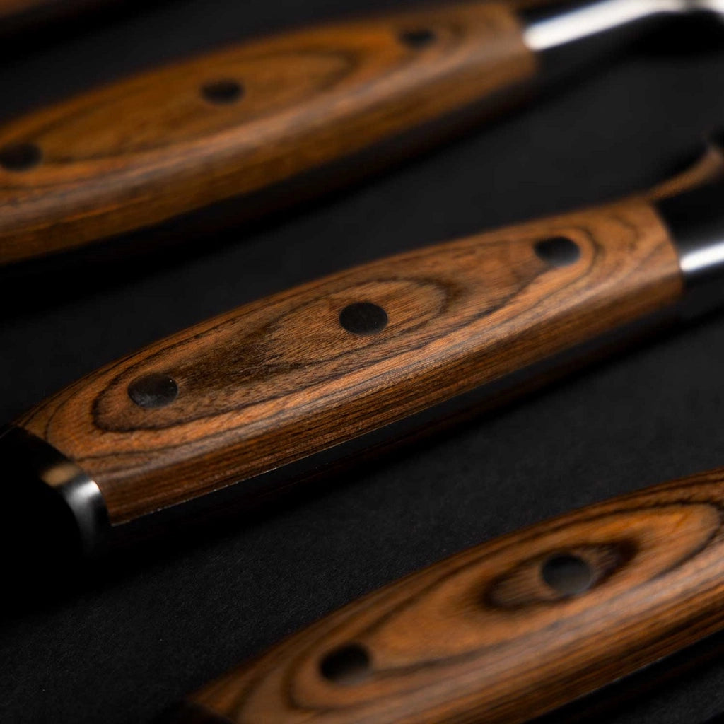 Nærbilde av Messermeister Avanta BBQ Knivsett trehåndtak, med naturlige årer og metallnagler, arrangert diagonalt på en mørk bakgrunn - ideelt for enhver grillkniv- eller BBQ-knivsamling.
