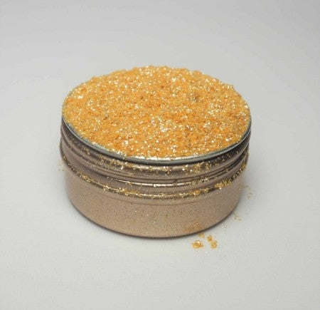 Eat Me Glitter Gold 20 ml fra Eco Lovers er en liten rund metallbeholder fylt med gullglitter, på en hvit overflate med litt glitter spredt rundt lokket.