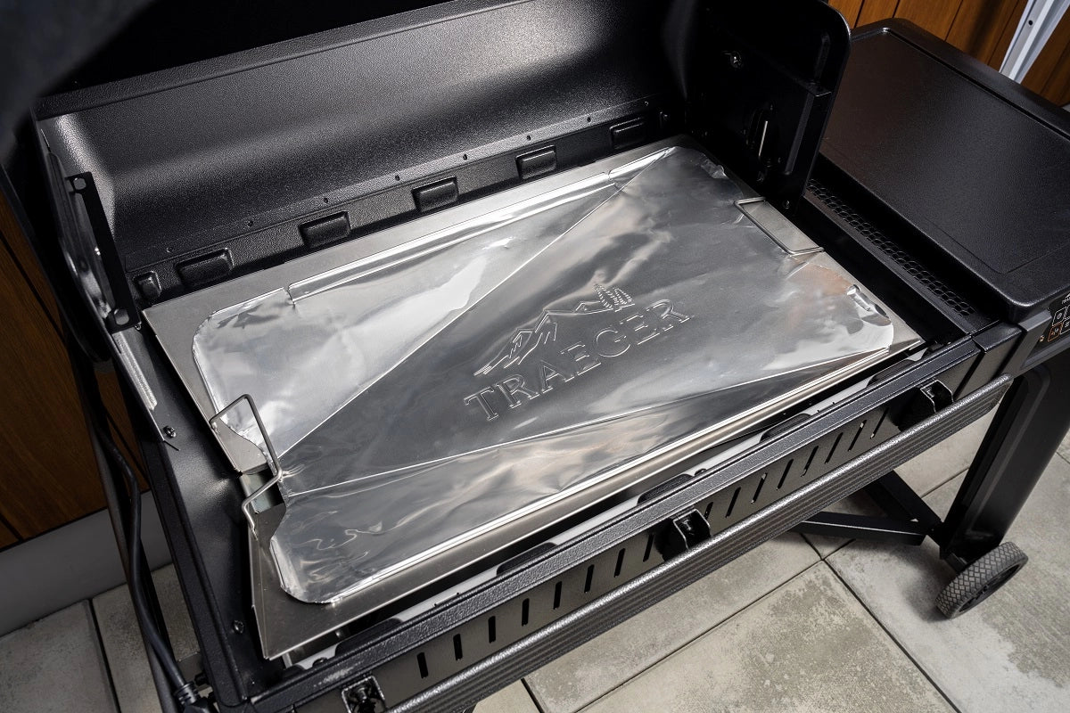 Åpne Traeger-grillen med et skinnende dryppbrett i metall med Traeger-logo - ideelt for bruk sammen med Traeger Drip Tray Liners, størrelse B 5-pk Pro780/IW885/Woodrige/Woodridge Pro - folieunderlag, for å holde grillen ren og enkel å vedlikeholde.
