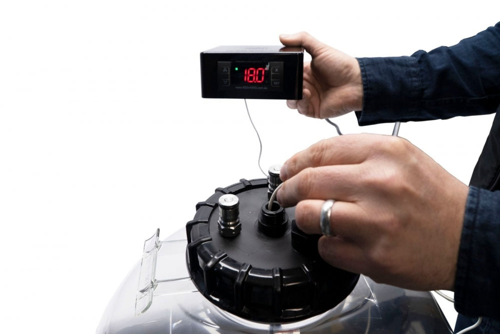 En person setter inn temperatursonder i det svarte lokket på en Keg King Apollo 30L Snub Nose-trykk-tank mens han holder et digitalt termometer som viser 18,0 °C.
