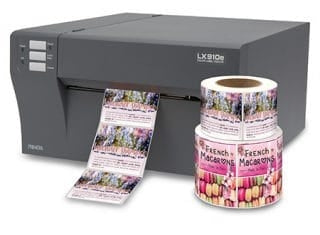 A Primera LX910e Etikettprinter (Bestillingsvare) fra Primera dispenserer etiketter, med tre ruller "French Macarons" fargeetiketter stablet ved siden av.