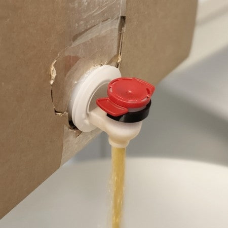 Nærbilde av Fresh Wort Kit Dispense Clip - Black Edition festet til en bag-in-box, som tapper en gulaktig væske gjennom den svarte tappen ned i et hvitt kar under.