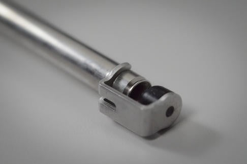 Nærbilde av en sylindrisk metallstang til Blichmann BeerGun flaskefyller fra Blichmann, som viser en maskinbearbeidet ende med hull og spor, plassert på en ren, lys overflate.