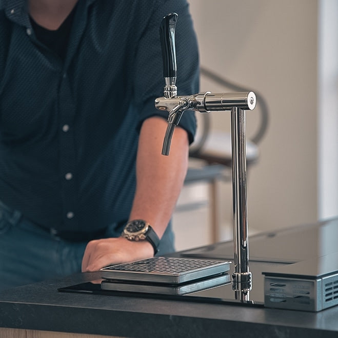 En person i mørk skjorte står ved siden av et Lindr PYGMY Pro Kitchen øltappsystem fra Lindr, installert på en benk, med den ene hånden hvilende nær dryppskålen.