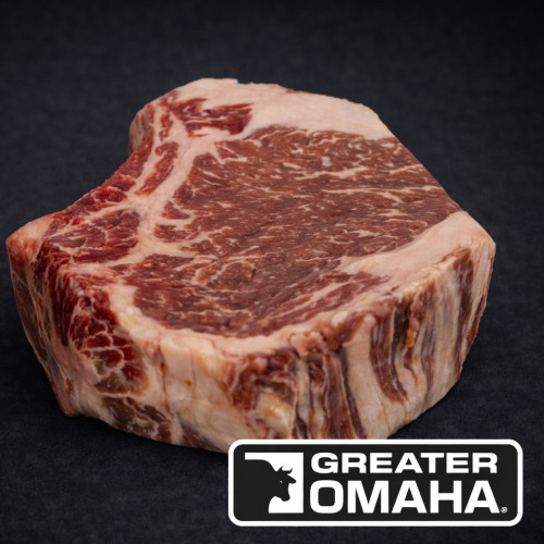 Et rått Storfe Entrecôte Greater Omaha 600 g stykke, rikt marmorert, vises på en mørk overflate med Greater Omaha-logoen nederst til høyre, noe som fremhever storfekjøttets førsteklasses kvalitet.