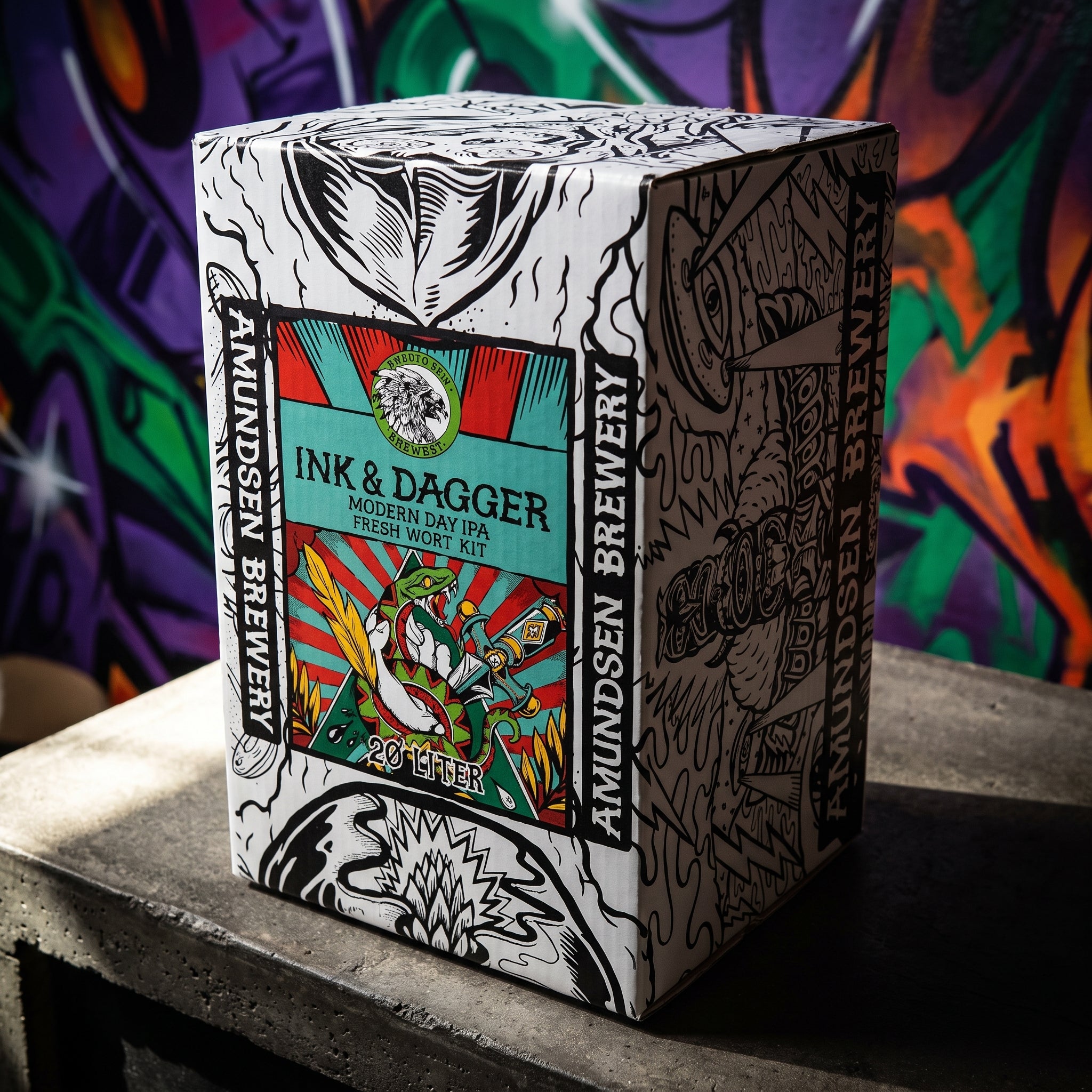 En eske med påskriften «Amundsen Ink & Dagger – 20L Fresh Wort Kit» står på et bord, med en fargerik graffitikunst i bakgrunnen som viser den kreative ånden ved Amundsen Bryggeri.