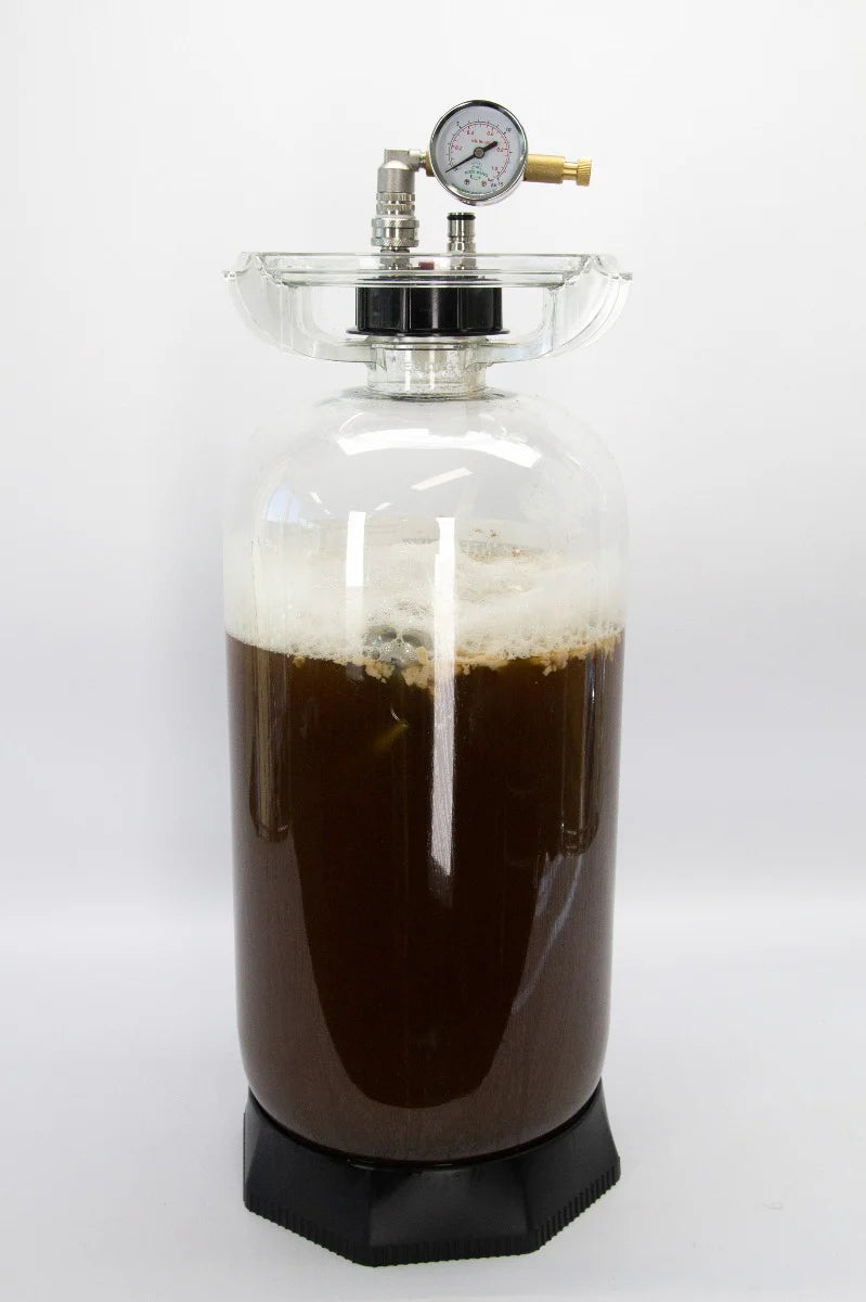 En Fermenter King Junior 20L trykktank og keg, fylt med mørk væske og skum og forseglet med et lokk og et trykkmåler, står på en svart sokkel mot en ensfarget hvit bakgrunn – et ideelt valg for trykkgjæring i hjemmebrygging.
