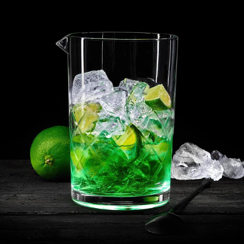 Lurch Blandeglass på 650 ml, fylt med grønn væske, isbiter og lime-båter, står på en mørk overflate ved siden av en hel lime, spredte isbiter og en cocktailskje – et ideelt oppsett for å blande rørte cocktailer eller servere dem i ditt favorittcocktailglass.