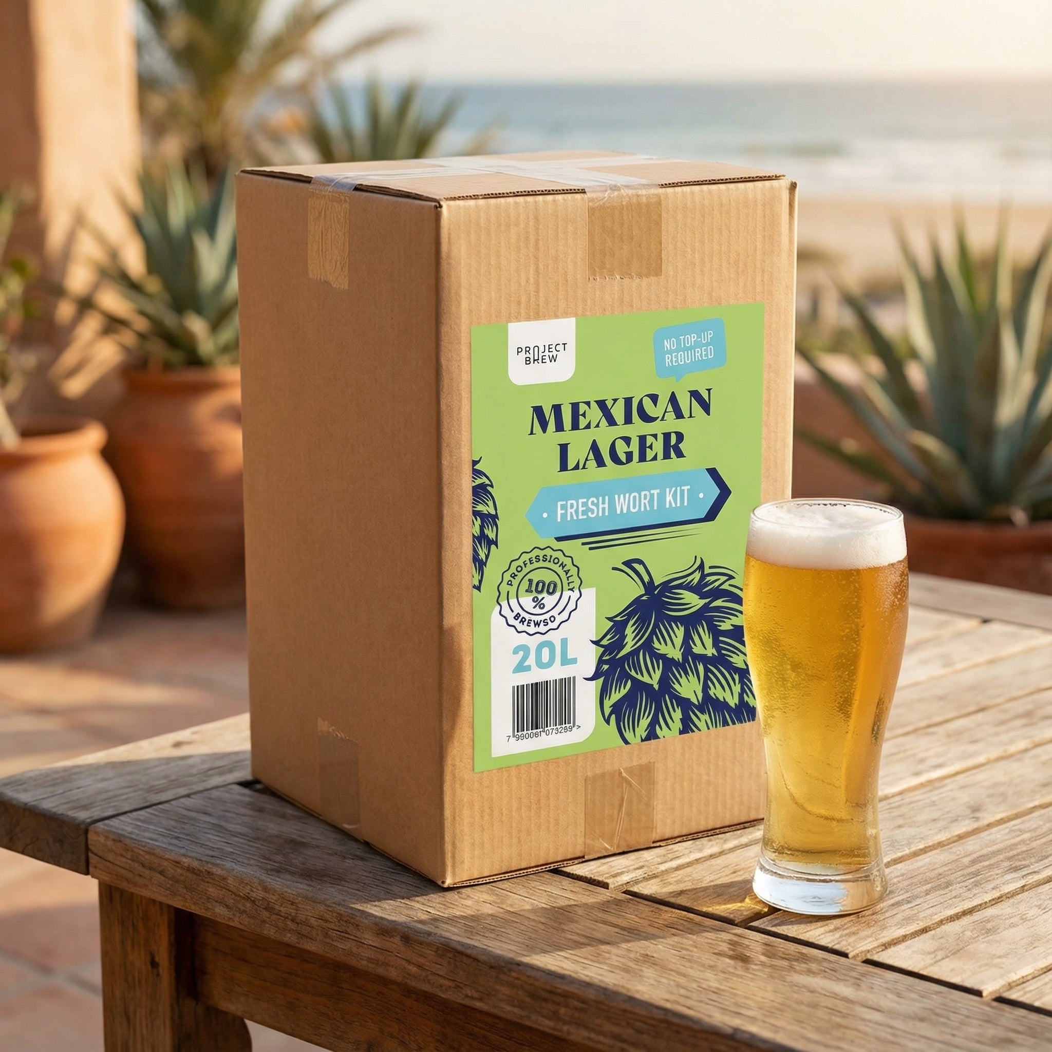 En eske merket "Austmann Mexican Lager - 20L Fresh Wort Kit" står på et trebord utendørs ved siden av et fylt halvliterglass med pils, med potteplanter og en strand i bakgrunnen.