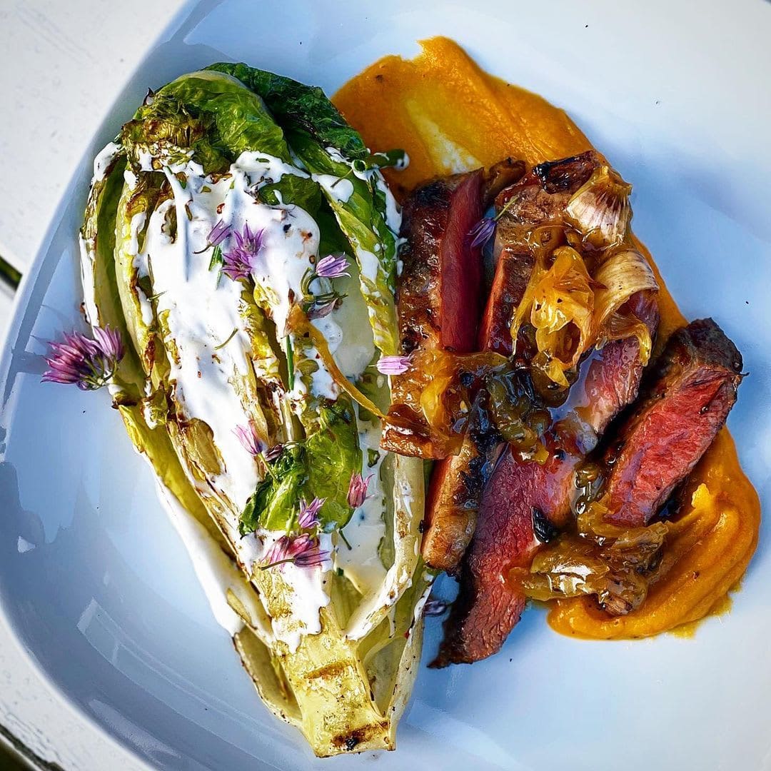 En tallerkenrett med grillet romaine med kremet dressing og urter, servert med skiver av Secreto Ibérico - Juan Pedro Domecq (Kr 630 per kg), karamellisert løk og appelsinsaus.