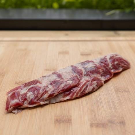 En rå Ibérico Pluma Spania (kr 700 per kg), en spansk spesialitet, hviler på et skjærebrett av tre med en uskarp grønn bakgrunn.