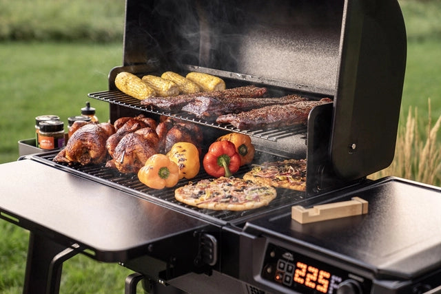 Traeger Woodridge Pelletsgrill er full av mais, ribbe, hele kyllinger, paprika og pizza. Røyken stiger til værs mens det digitale displayet viser 225°F, noe som gir ekte vedfyrt grillsmak.