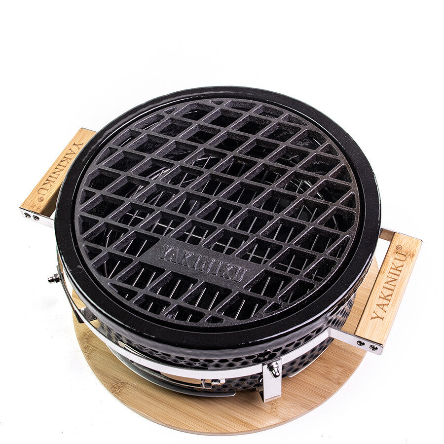 YAKINIKU Shichirin Støpejernsrist Rund, Medium har en rund grill med svart støpejernsrist, trehåndtak merket YAKINIKU, og står på en sirkulær trefot, vist ovenfra.